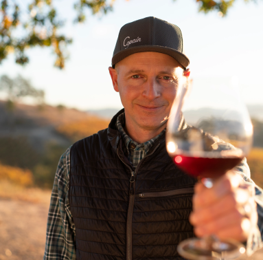 Copain Wines' Winemaker, Ryan Zepaltas, holding out a glass of Copain red wine.